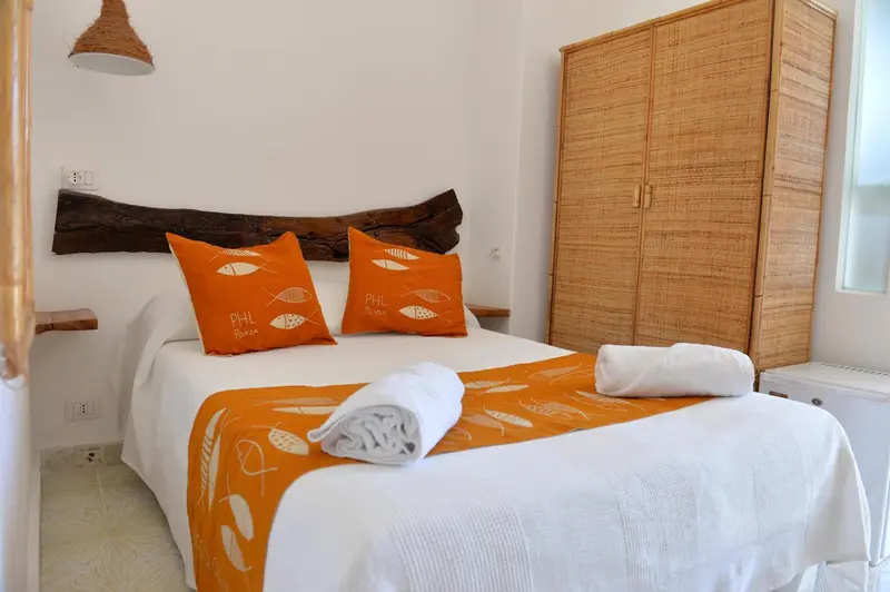 Lit préparé avec des coussins et une couverture orange dans une chambre lumineuse.