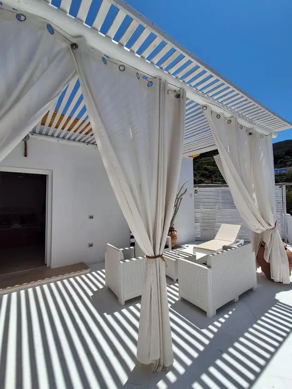 Espace de détente ombragé avec mobilier blanc et sol rayé.