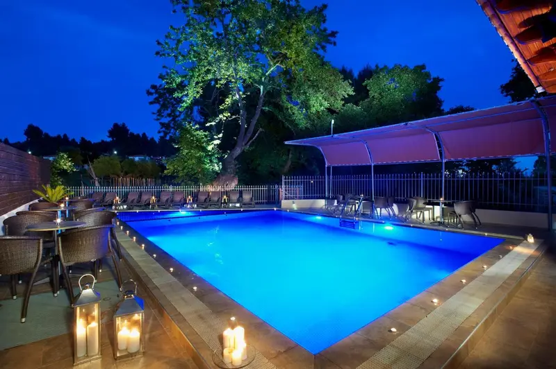 Piscine illuminée avec chaises longues et tables en soirée.