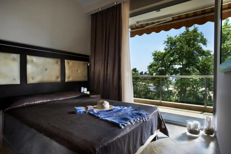Une chambre avec un grand lit donnant sur une terrasse ensoleillée.