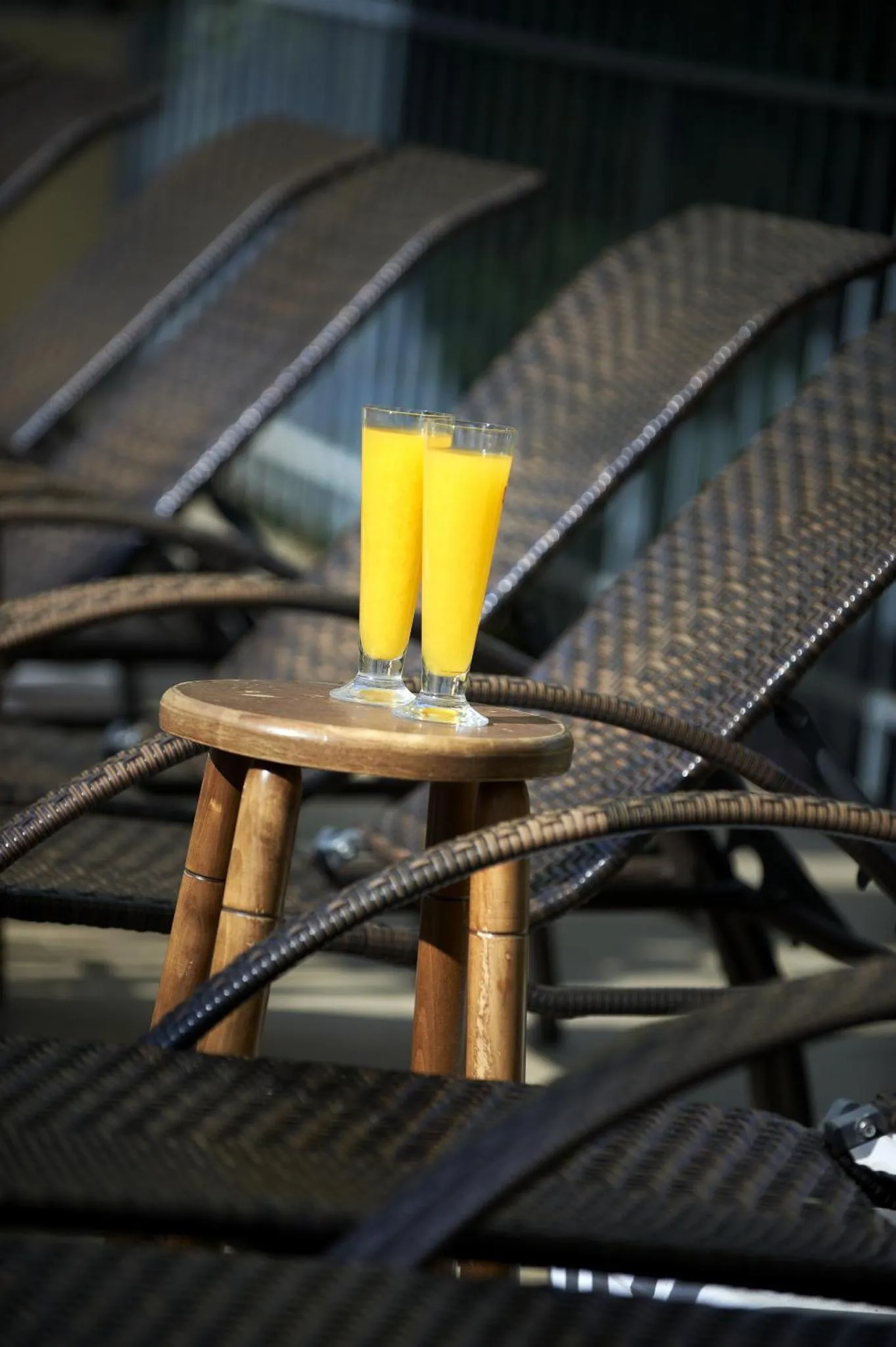 Deux verres de jus d'orange sont posés sur une table basse en bambou, entourés de transats.