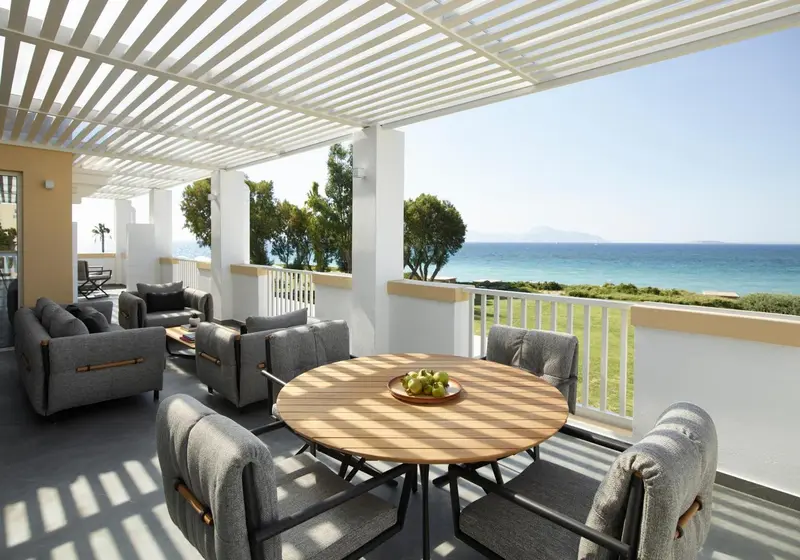 Terrasse ombragée avec mobilier de jardin et vue sur la mer.