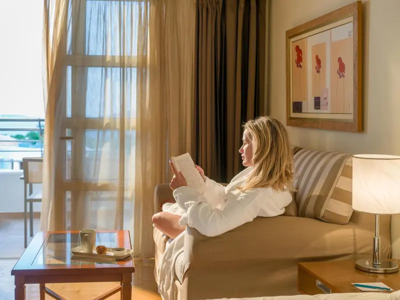 Une femme lit un livre assise sur un canapé dans une pièce lumineuse.