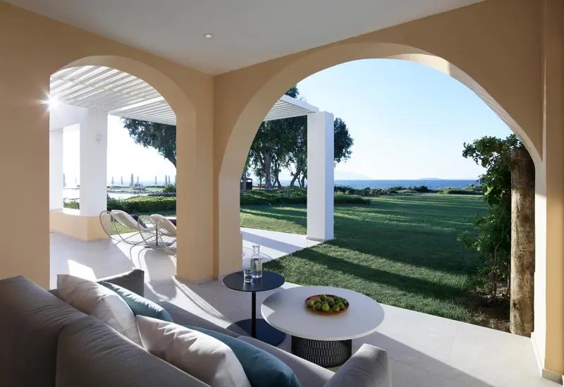 Un espace de détente extérieur avec canapés et table basse offre une vue sur un jardin verdoyant et la mer.