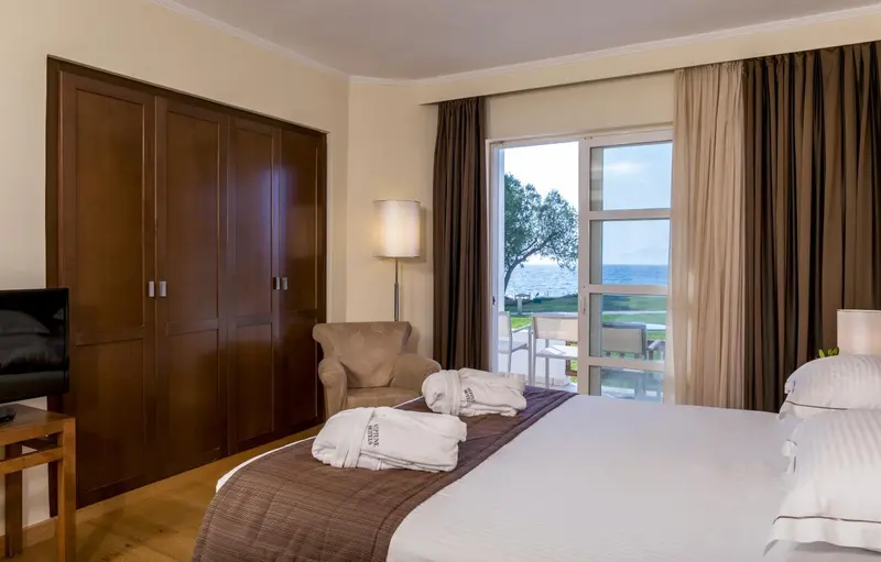 Une chambre lumineuse avec un lit fait et un fauteuil près d'une fenêtre donnant sur la mer.