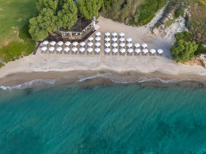 Vue aérienne d'une plage avec des transats alignés et une zone herbeuse.