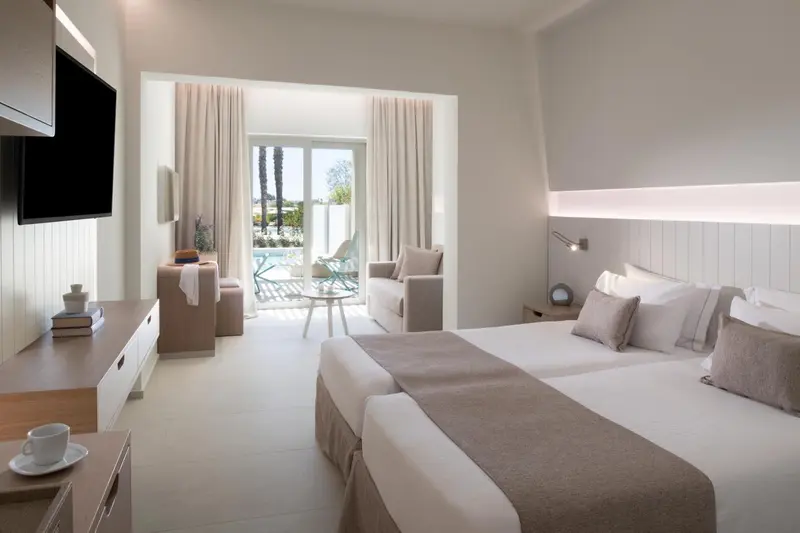 Chambre lumineuse avec un lit double et un coin salon donnant sur une terrasse.