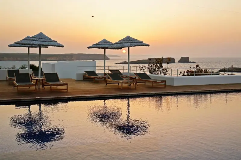 Terrasse avec transats et piscine au bord de la mer au coucher du soleil.