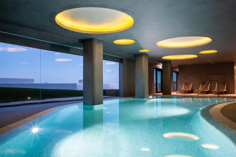 Une piscine intérieure éclairée par des luminaires circulaires au plafond.