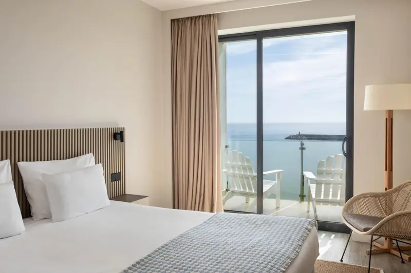 Une chambre lumineuse avec un grand lit donnant sur une vue mer et une terrasse.