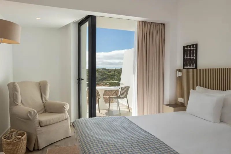 Une chambre lumineuse s'ouvre sur un balcon avec vue sur la végétation.