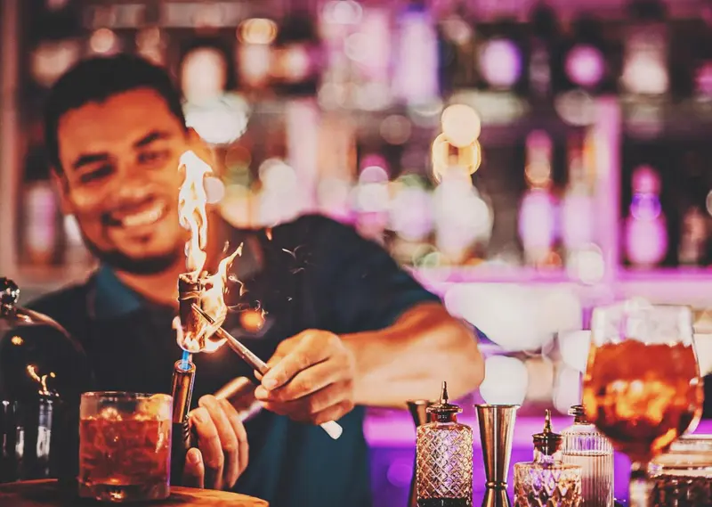 Un barman prépare un cocktail enflammé au comptoir.