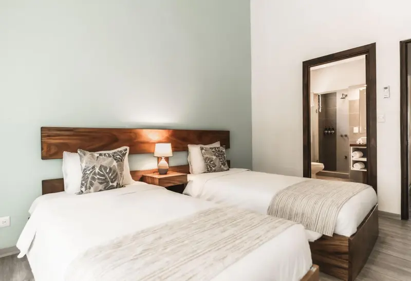 Une chambre lumineuse avec deux lits simples et une salle de bain visible au fond.