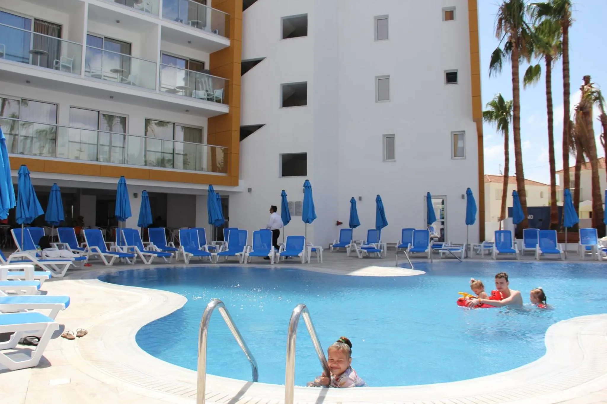 Une piscine avec des transats bleus et des palmiers en arrière-plan.