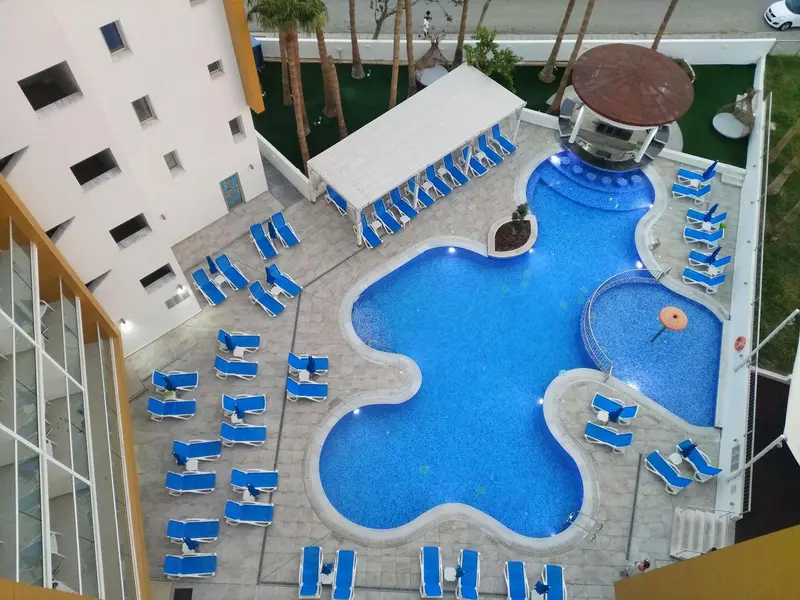 Vue aérienne d'une piscine d'hôtel avec des transats bleus et un espace vert.