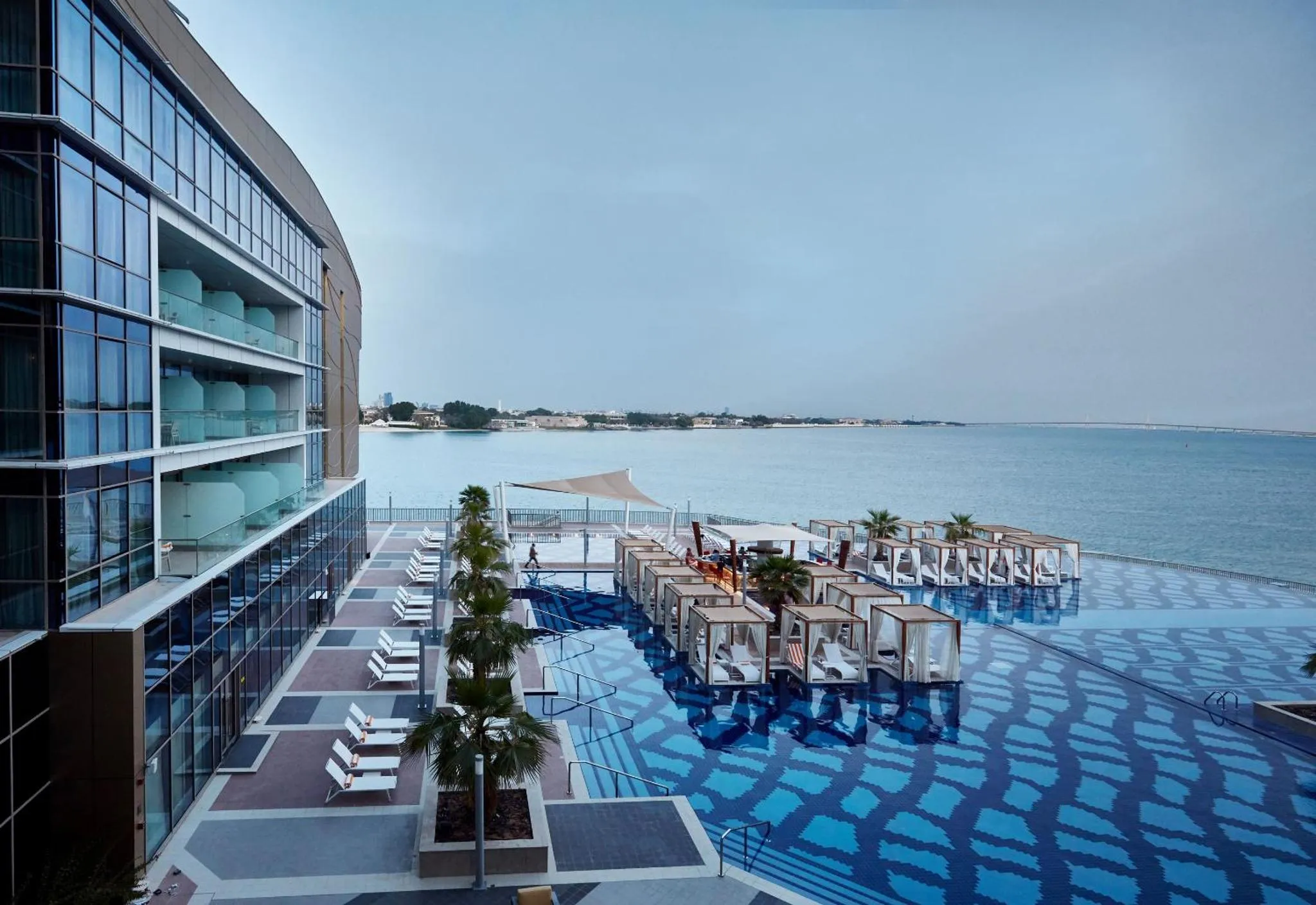 Vue d'une piscine avec des cabanas et un bâtiment moderne en bord de mer.