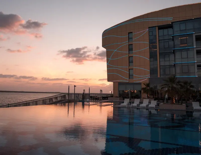 Bâtiment moderne au bord de l'eau avec piscine à débordement au premier plan.