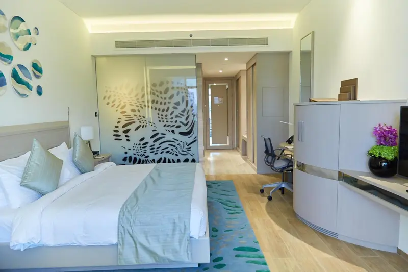 Chambre lumineuse avec un grand lit et un espace bureau.
