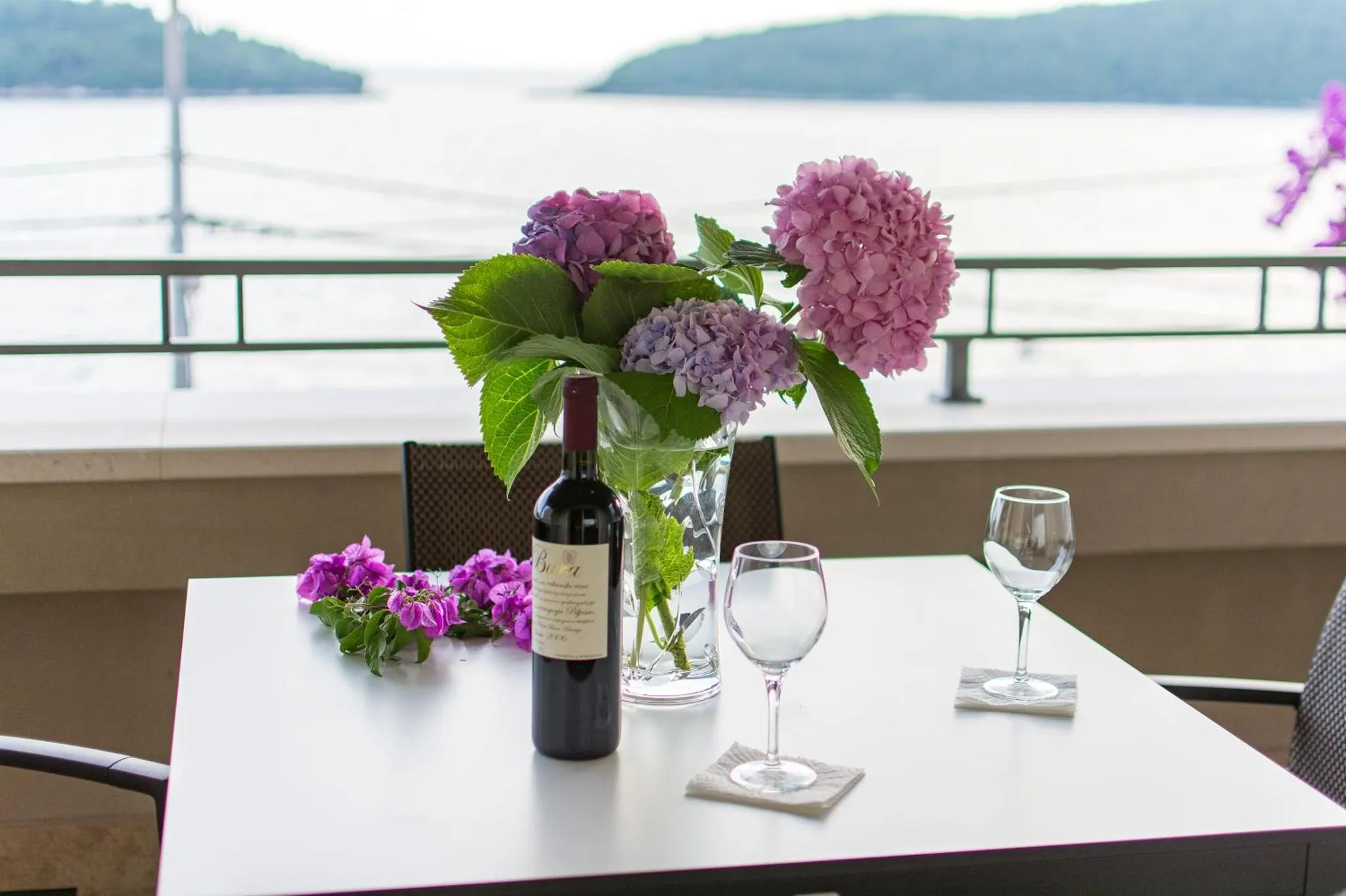 Une table est mise avec une bouteille de vin et des verres, devant une vue sur la mer.