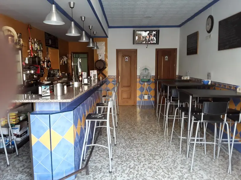 Un comptoir de bar avec des tabourets et des bouteilles est visible dans une pièce lumineuse.