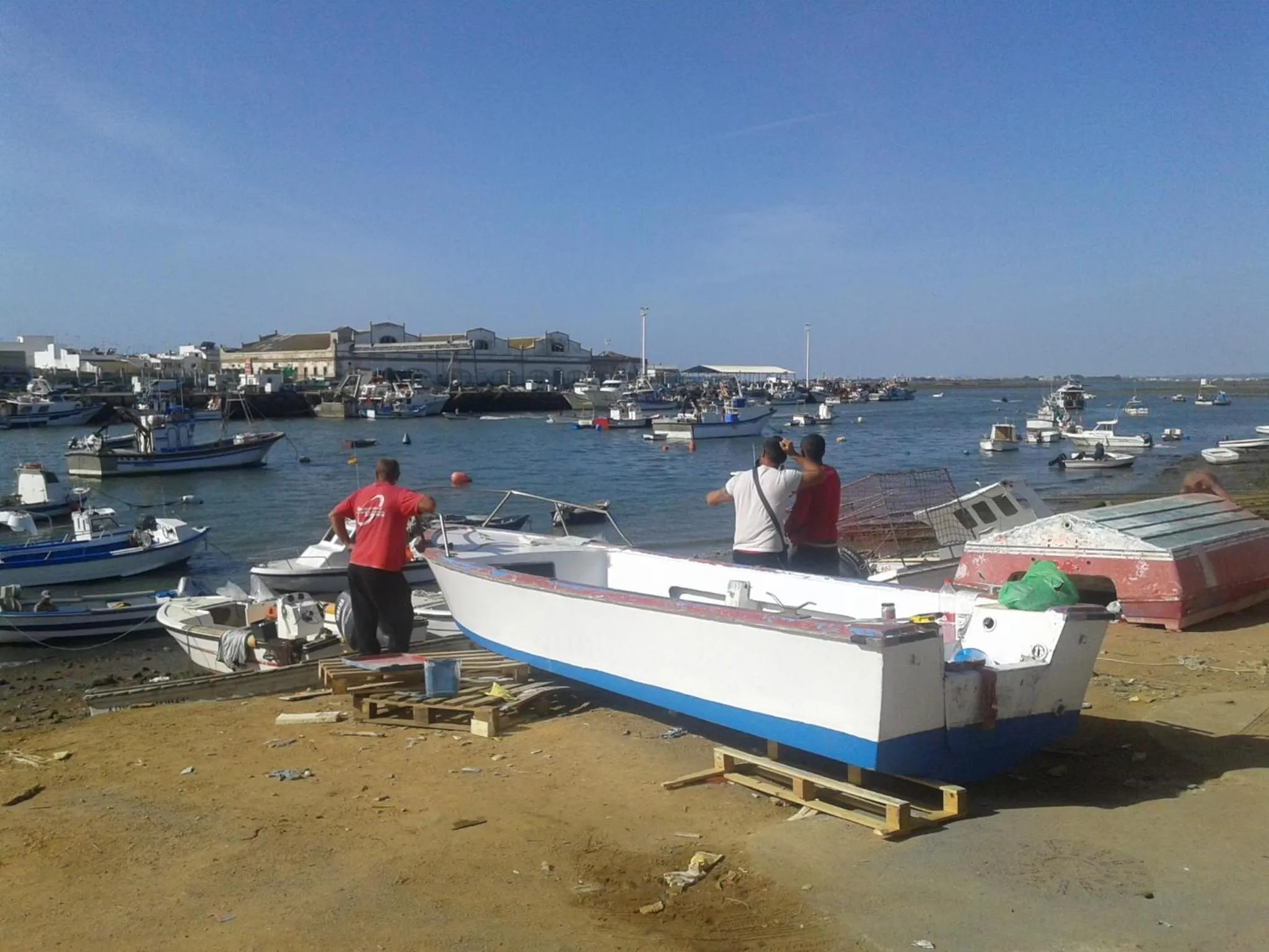 Des hommes travaillent sur un bateau à quai, avec des embarcations amarrées en arrière-plan.