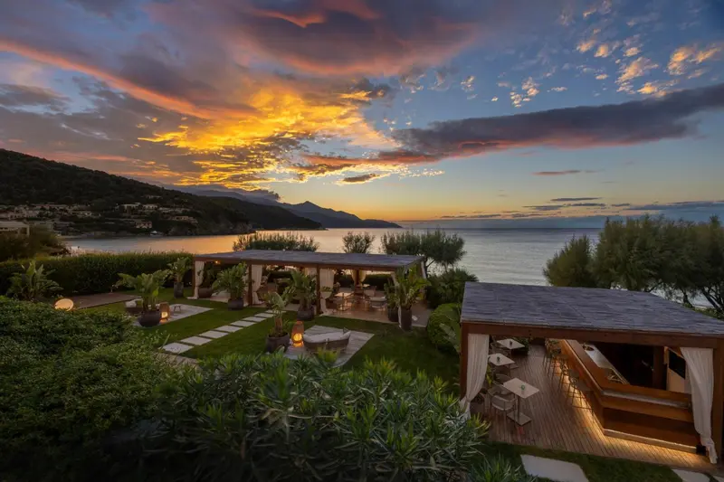 Terrasse avec mobilier de jardin et vue sur la mer au coucher du soleil.