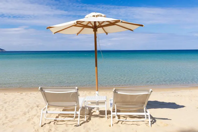 Deux transats blancs et une table basse sur une plage de sable fin, face à une mer turquoise.