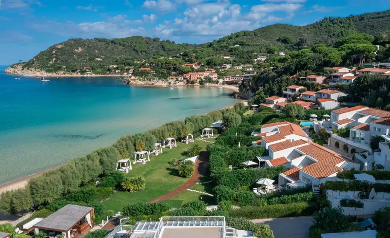 Vue aérienne d'un complexe hôtelier blanc et rouge au bord d'une crique turquoise.