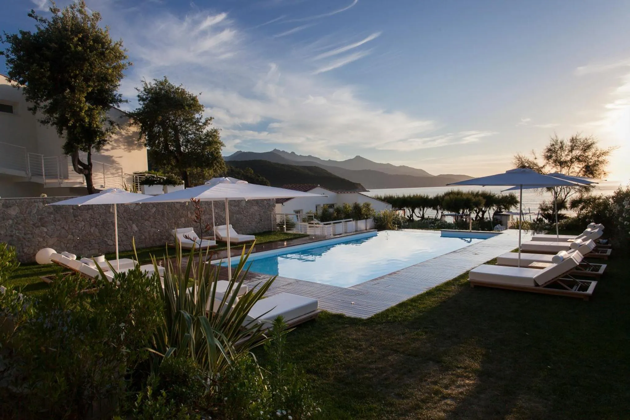 Une piscine rectangulaire bordée de transats blancs, avec une vue sur la mer et les montagnes.