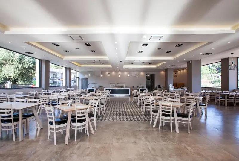 Une grande salle lumineuse est aménagée avec des tables et des chaises blanches.
