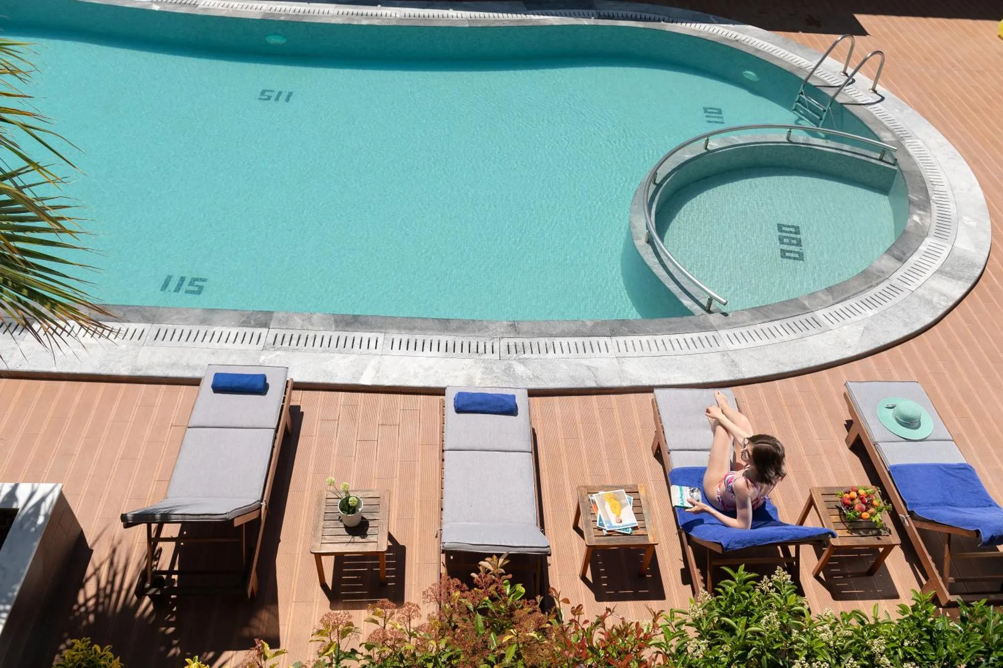 Transats et table basse au bord d'une piscine rectangulaire et d'un jacuzzi.