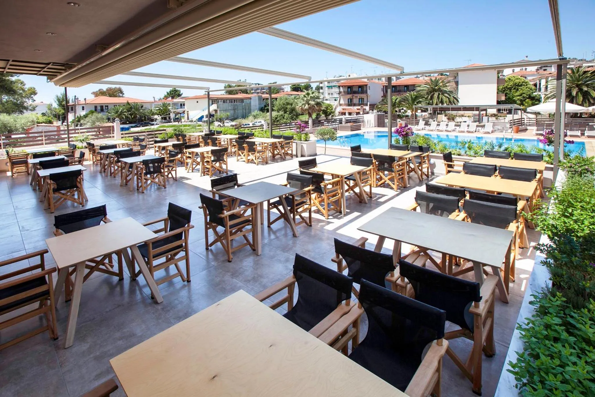 Terrasse ombragée avec tables et chaises près d'une piscine.