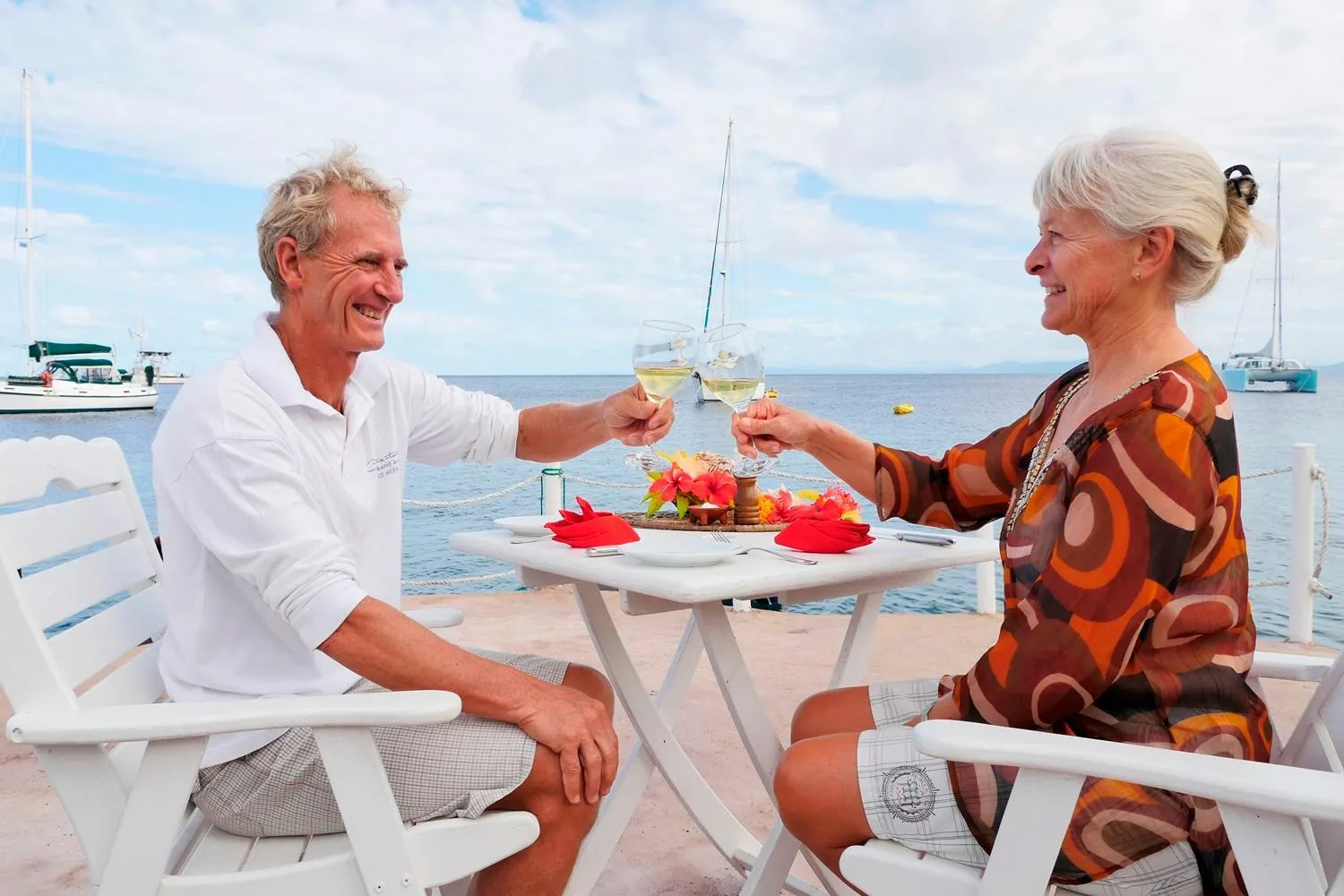 Un couple trinque avec des verres de vin assis à une table en extérieur face à la mer.