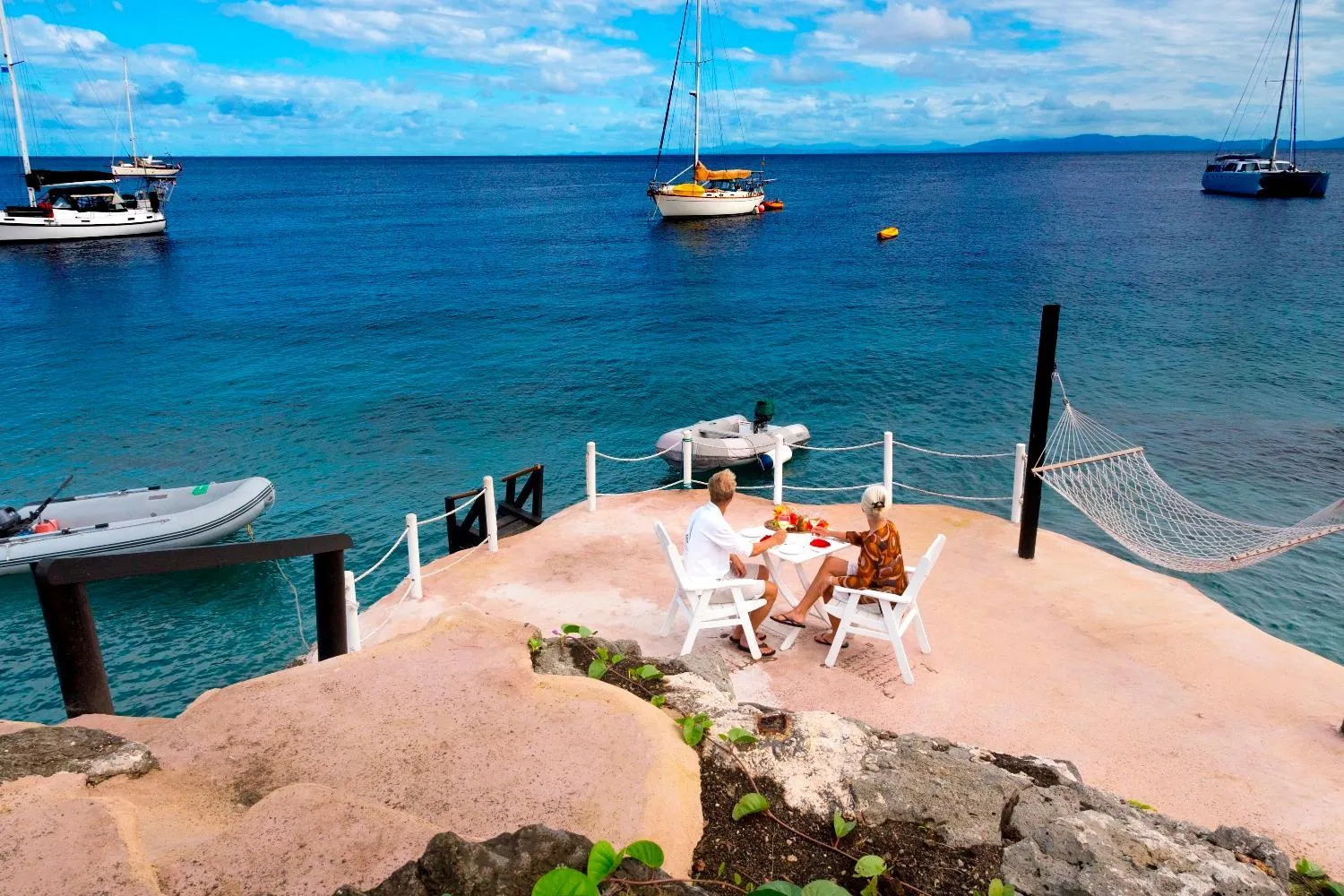 Deux personnes sont assises à une table sur une terrasse surplombant la mer.