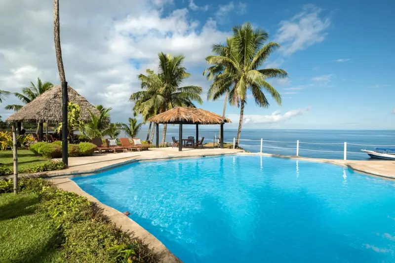Piscine turquoise bordée d'une terrasse ensoleillée avec vue sur la mer.