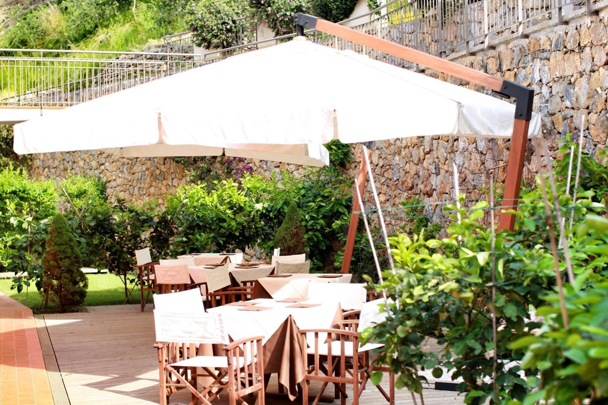 Tables dressées à l'ombre d'un parasol sur une terrasse ensoleillée.