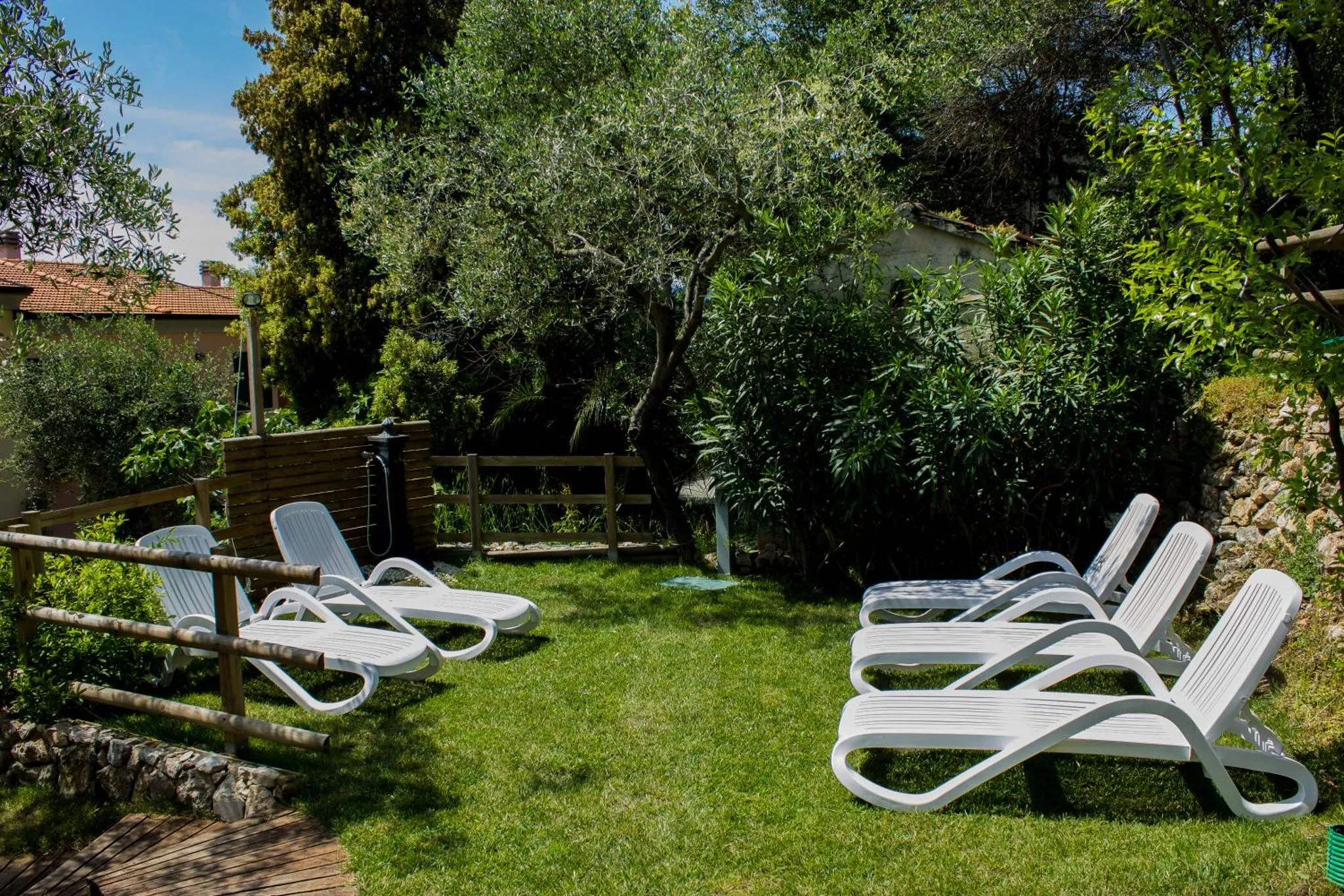 Transats blancs disposés sur une pelouse verdoyante dans un jardin ombragé.