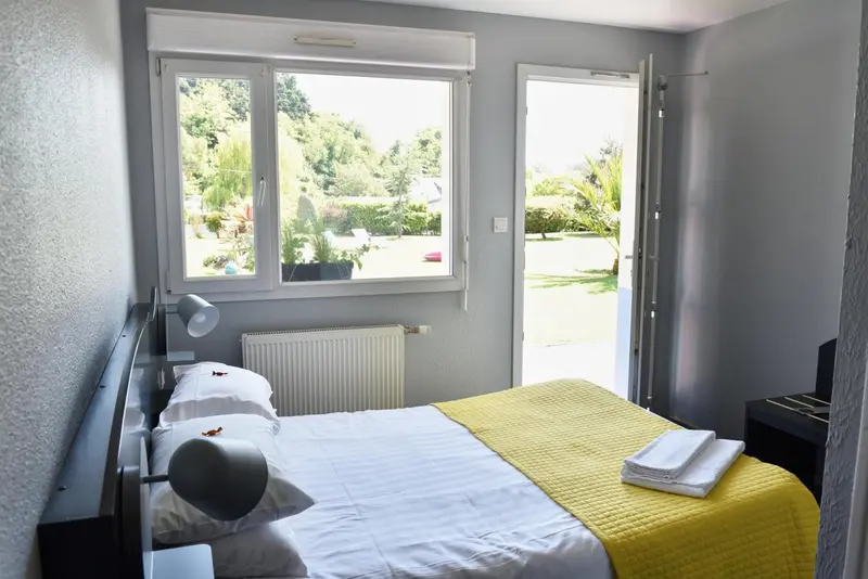 Une chambre lumineuse avec un lit jaune et une vue sur un jardin verdoyant.