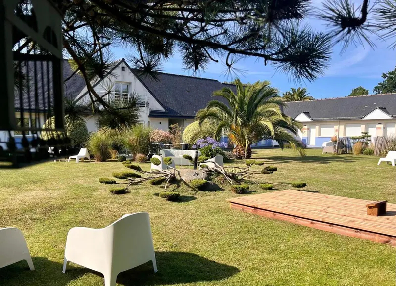 Vue d'un jardin verdoyant avec des bâtiments blancs en arrière-plan.