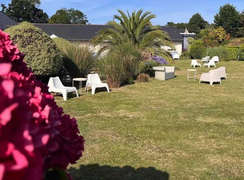 Un jardin verdoyant avec des meubles de jardin blancs et des arbustes fleuris.