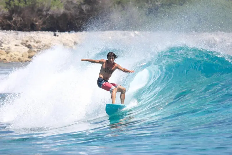 Un surfeur chevauche une vague turquoise dans une eau claire.