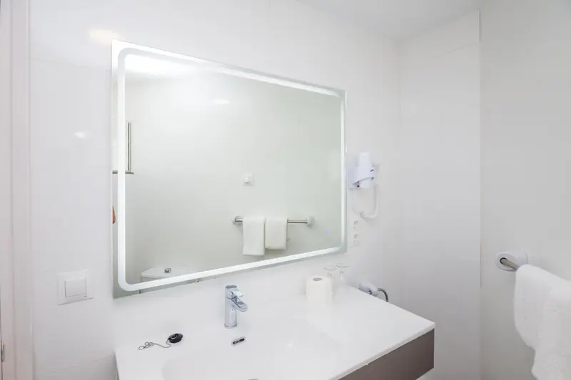 Une salle de bain lumineuse avec un grand miroir et un lavabo.