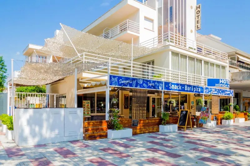 Façade d'un bâtiment blanc avec une pergola ombragée et des tables.