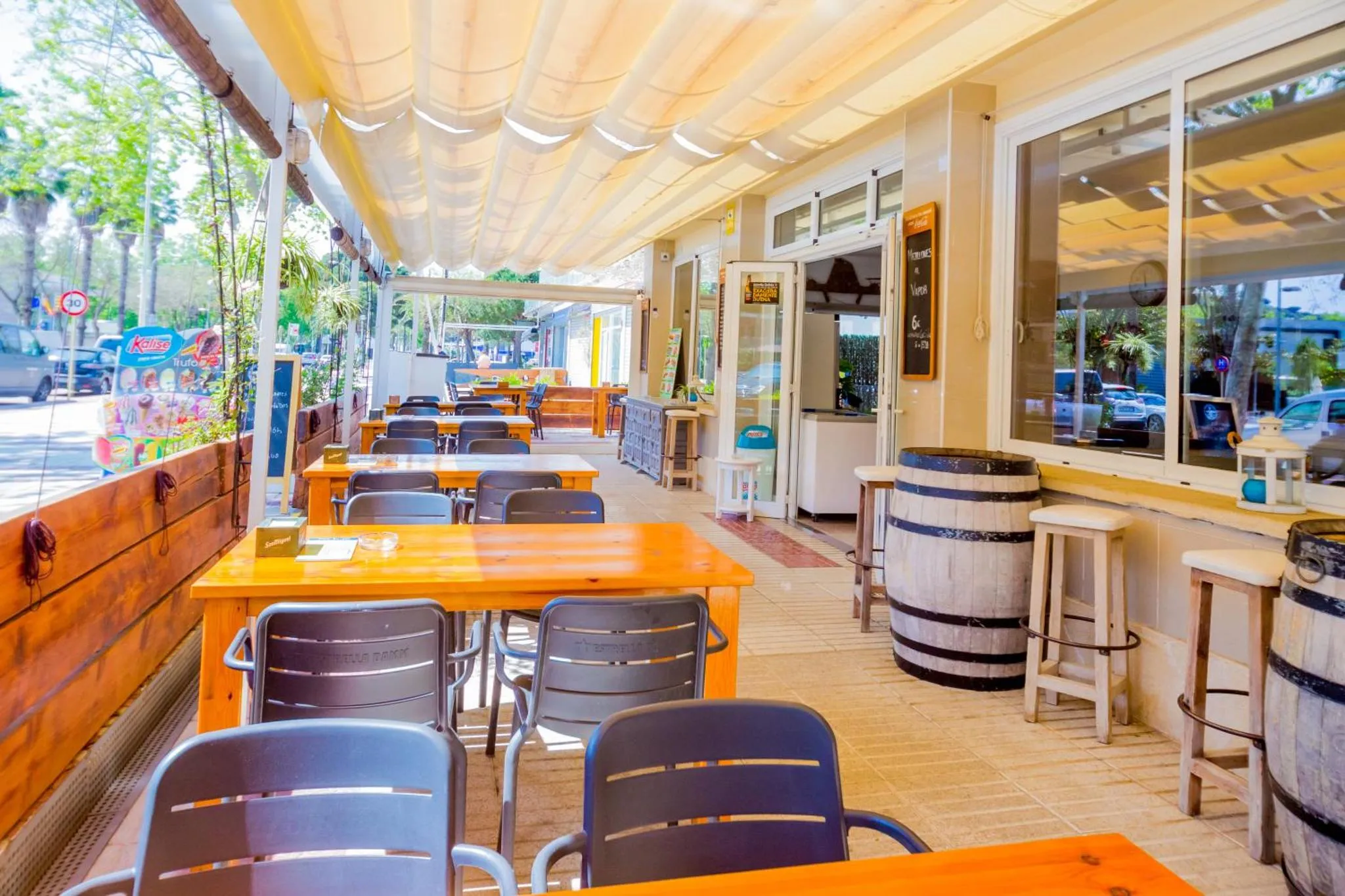 Terrasse ombragée avec tables et chaises en bois, près d'un bar extérieur.