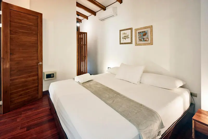 Une chambre lumineuse avec un grand lit recouvert d'une courtepointe et de coussins blancs.