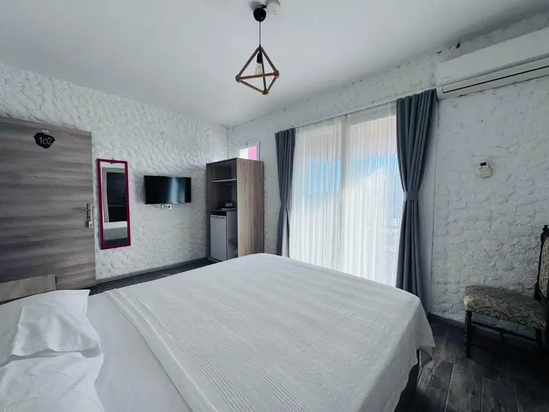 Chambre lumineuse avec un grand lit et une fenêtre drapée.