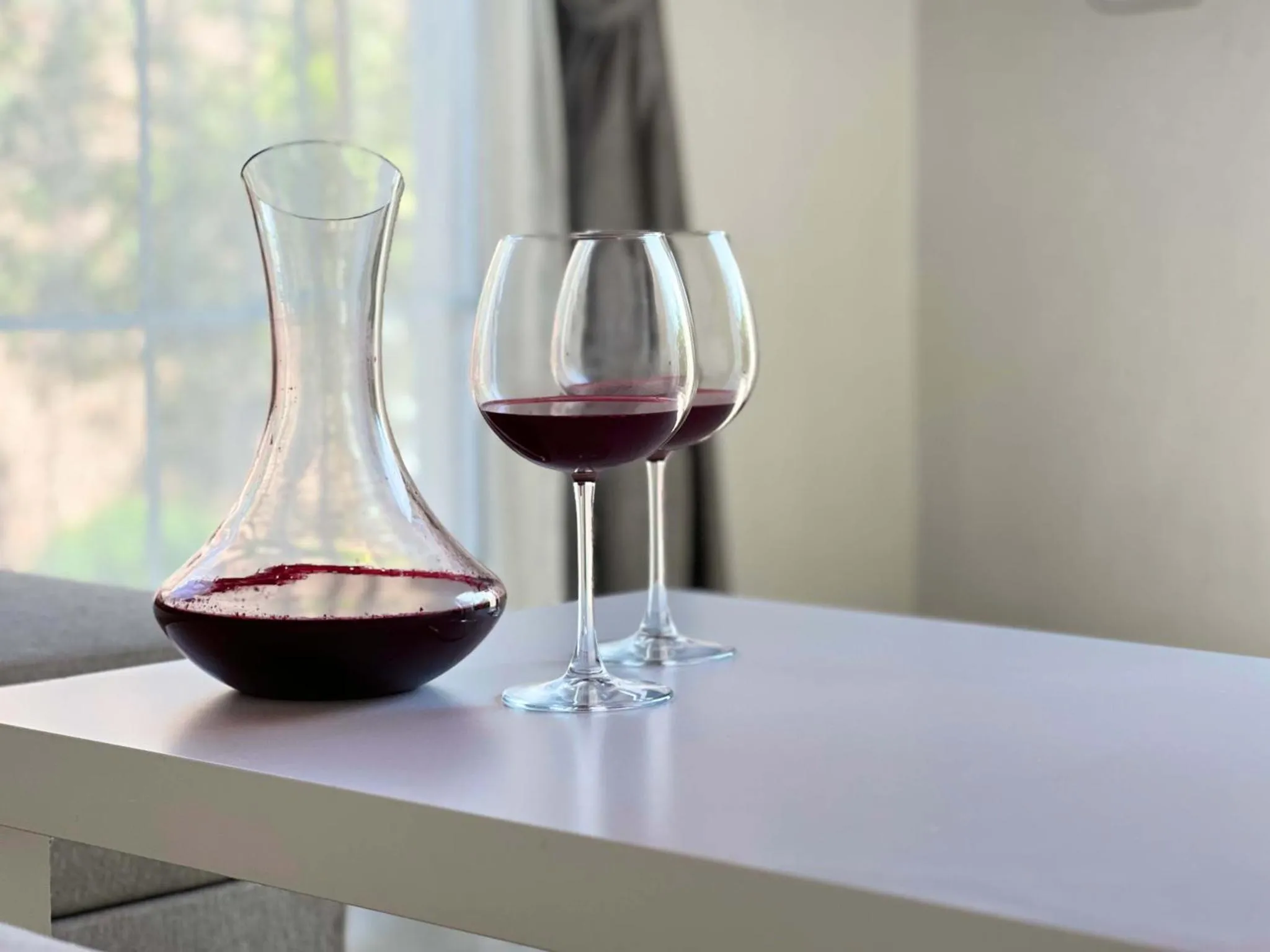 Une carafe et deux verres de vin rouge sont posés sur une table claire.