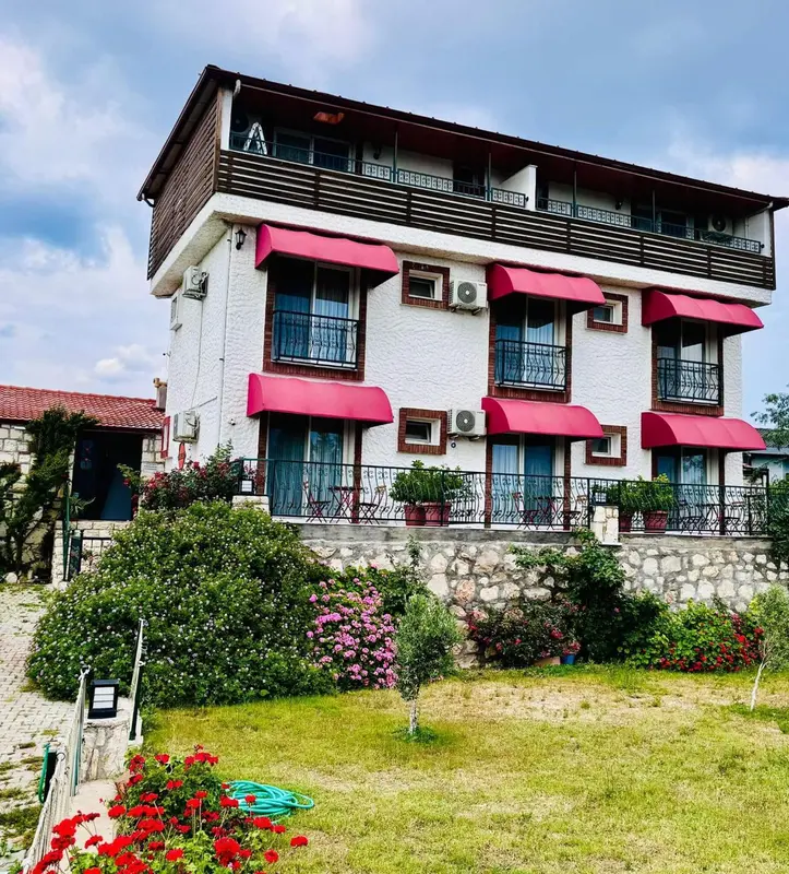 Bâtiment blanc à plusieurs étages avec des balcons et des auvents roses, entouré de végétation.