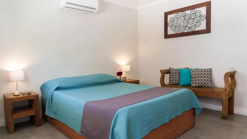 Une chambre lumineuse avec un grand lit recouvert d'une courtepointe turquoise et d'un plaid violet.