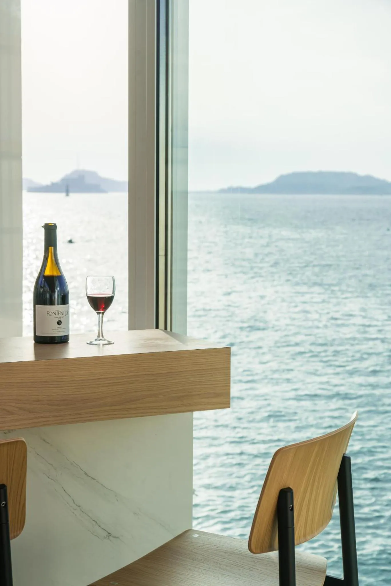 Une bouteille de vin et un verre sont posés sur un comptoir face à la mer.